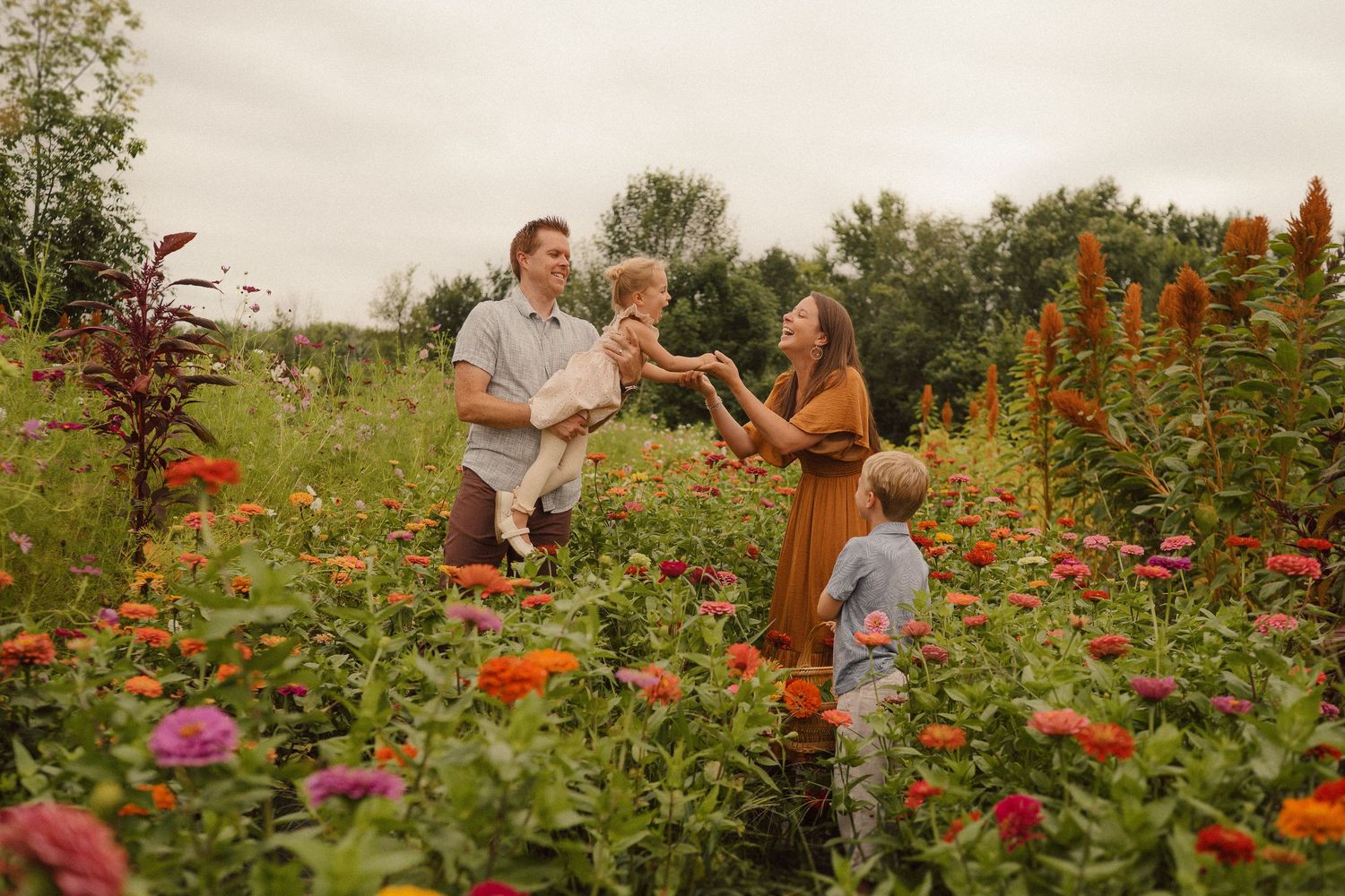 A candid family moment together in a vibrant flower garden filled with pink and orange blooms on a summer day.