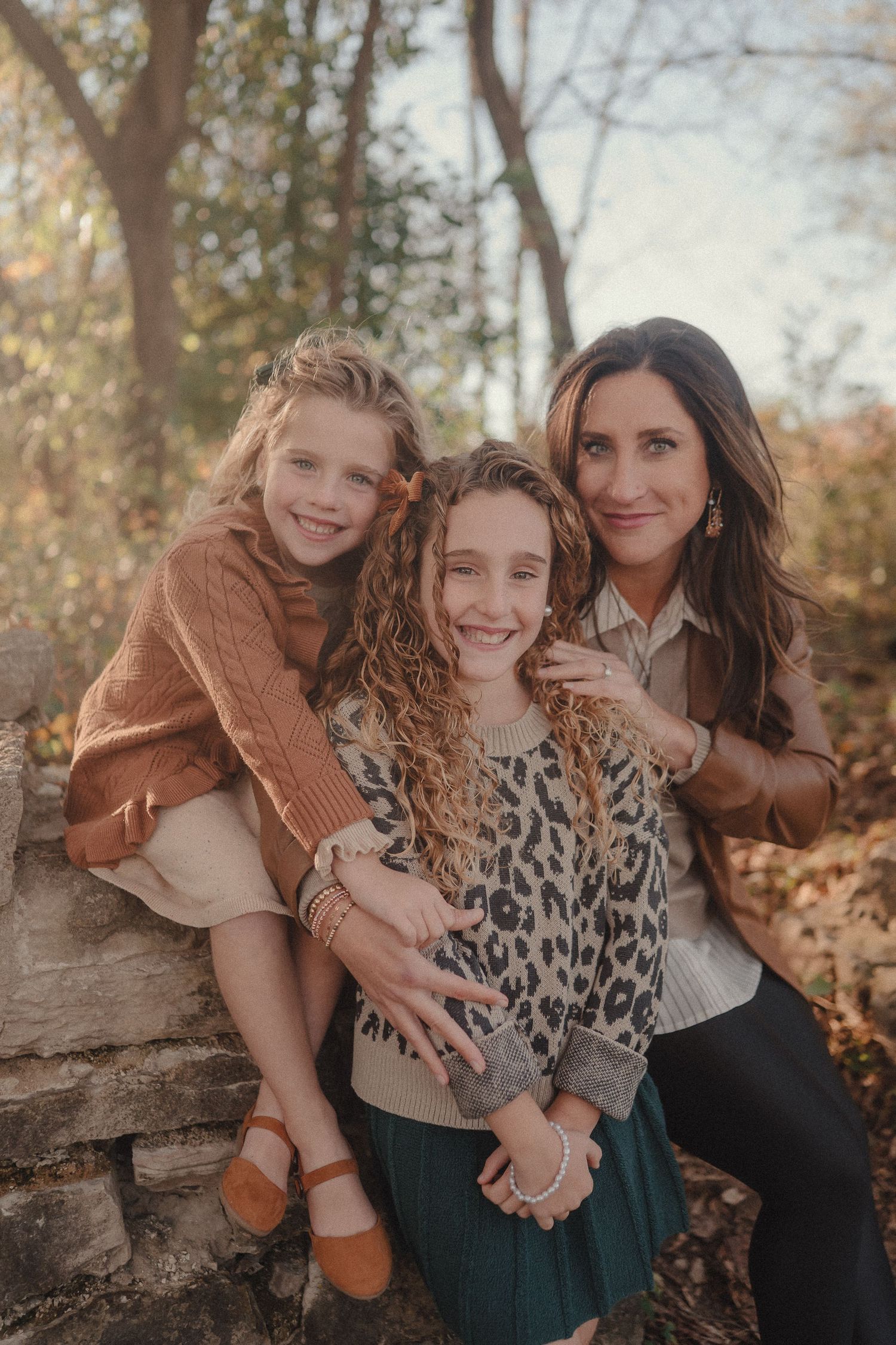 Candid family moment on stone wall with autumn foliage in background during sunset photoshoot.