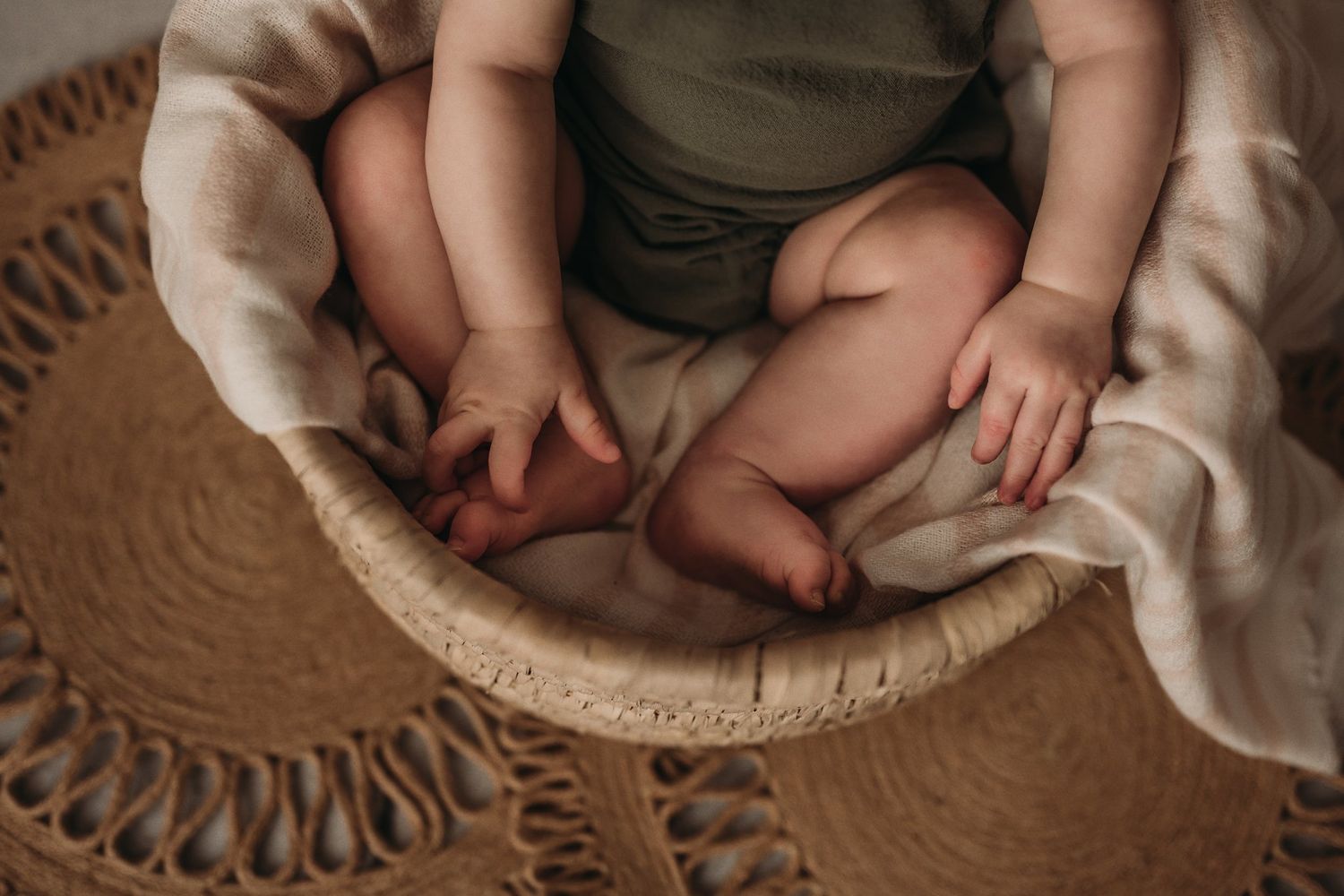Close-up of tiny feet and legs in woven basket with cream fabric.