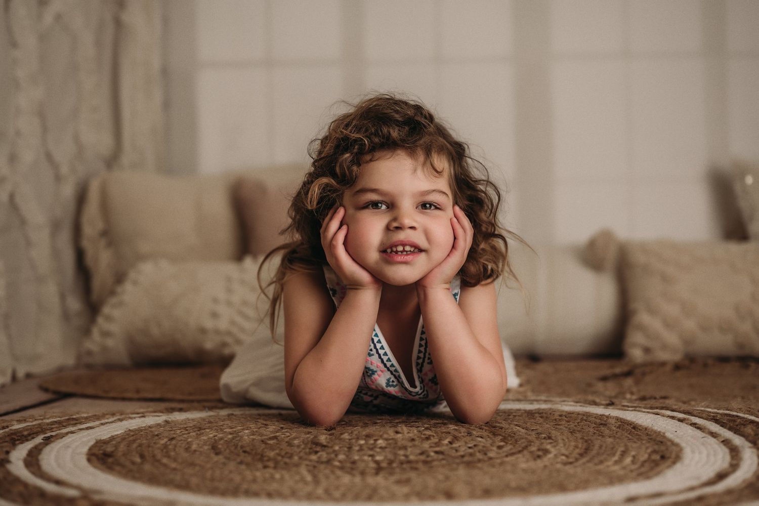 Child lying on patterned rug in casual pose with hands under chin.