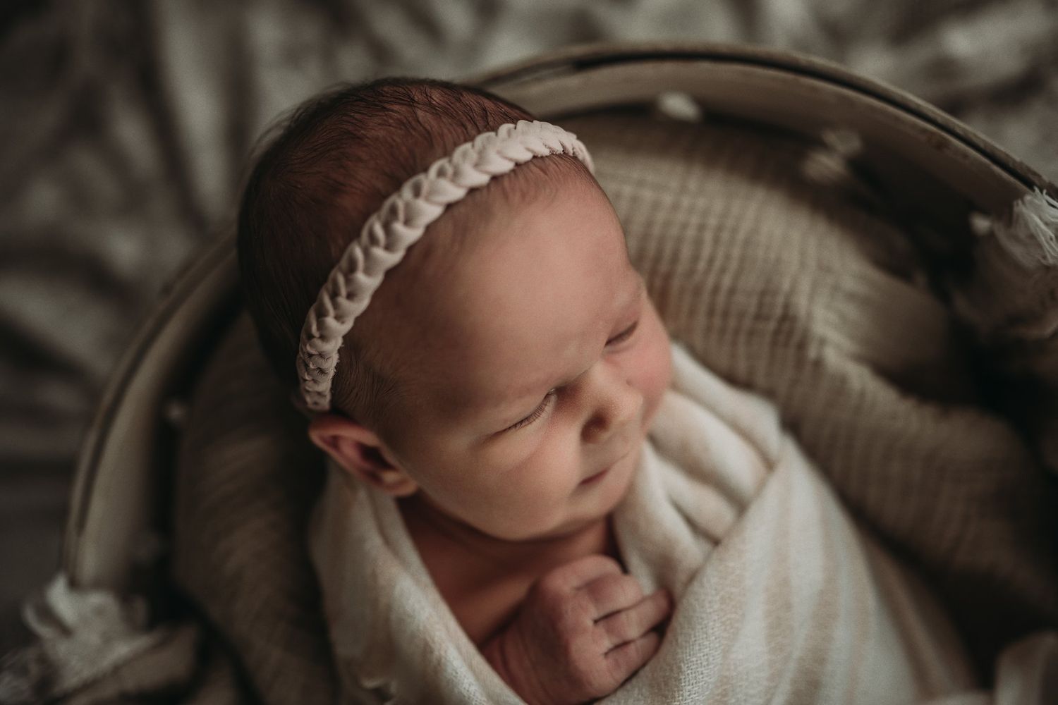 Close up of sleeping infant in cream wrap and braided headband against textured background.