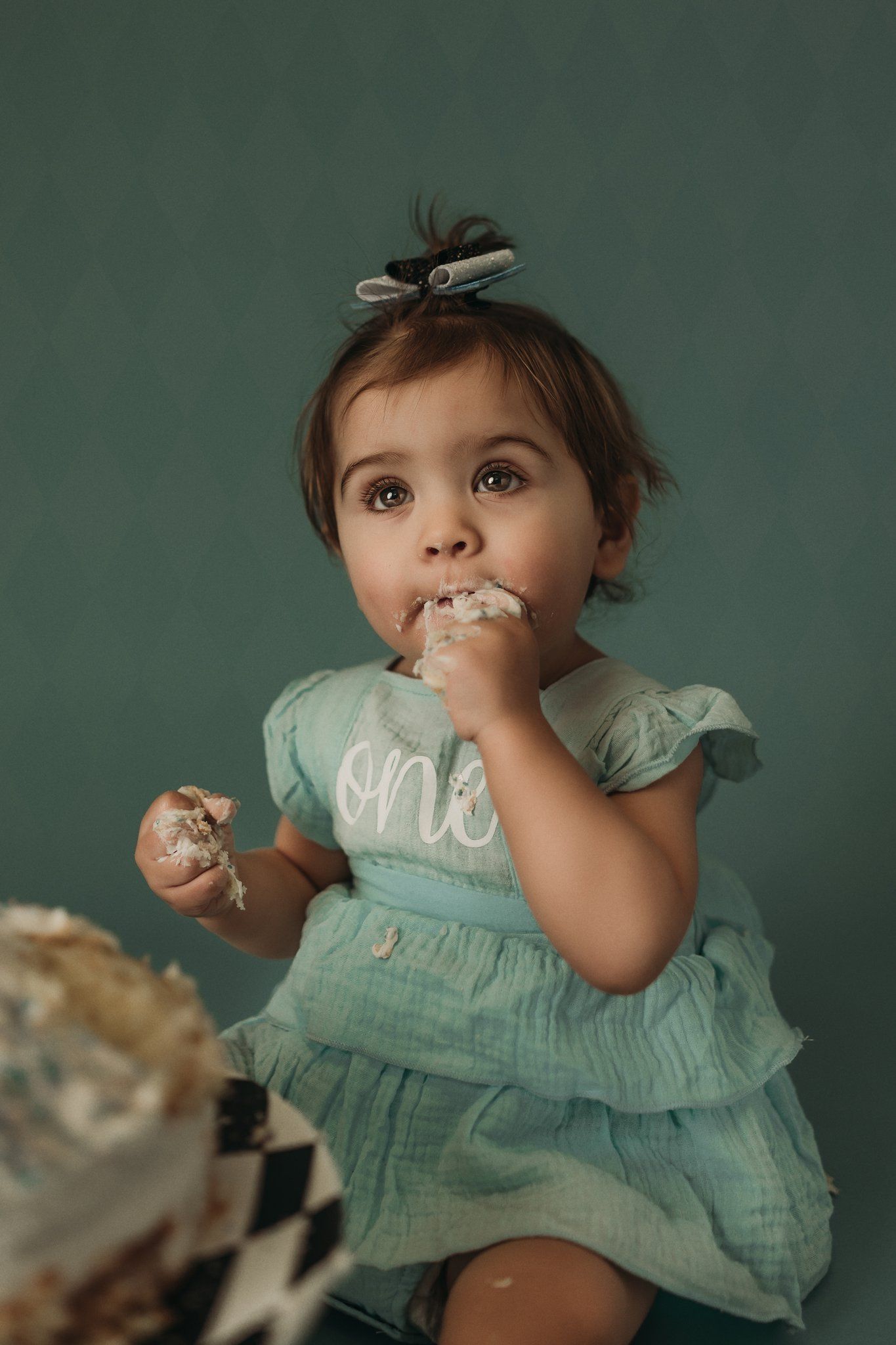A candid moment of cake tasting during a first birthday photoshoot with a mint green dress.
