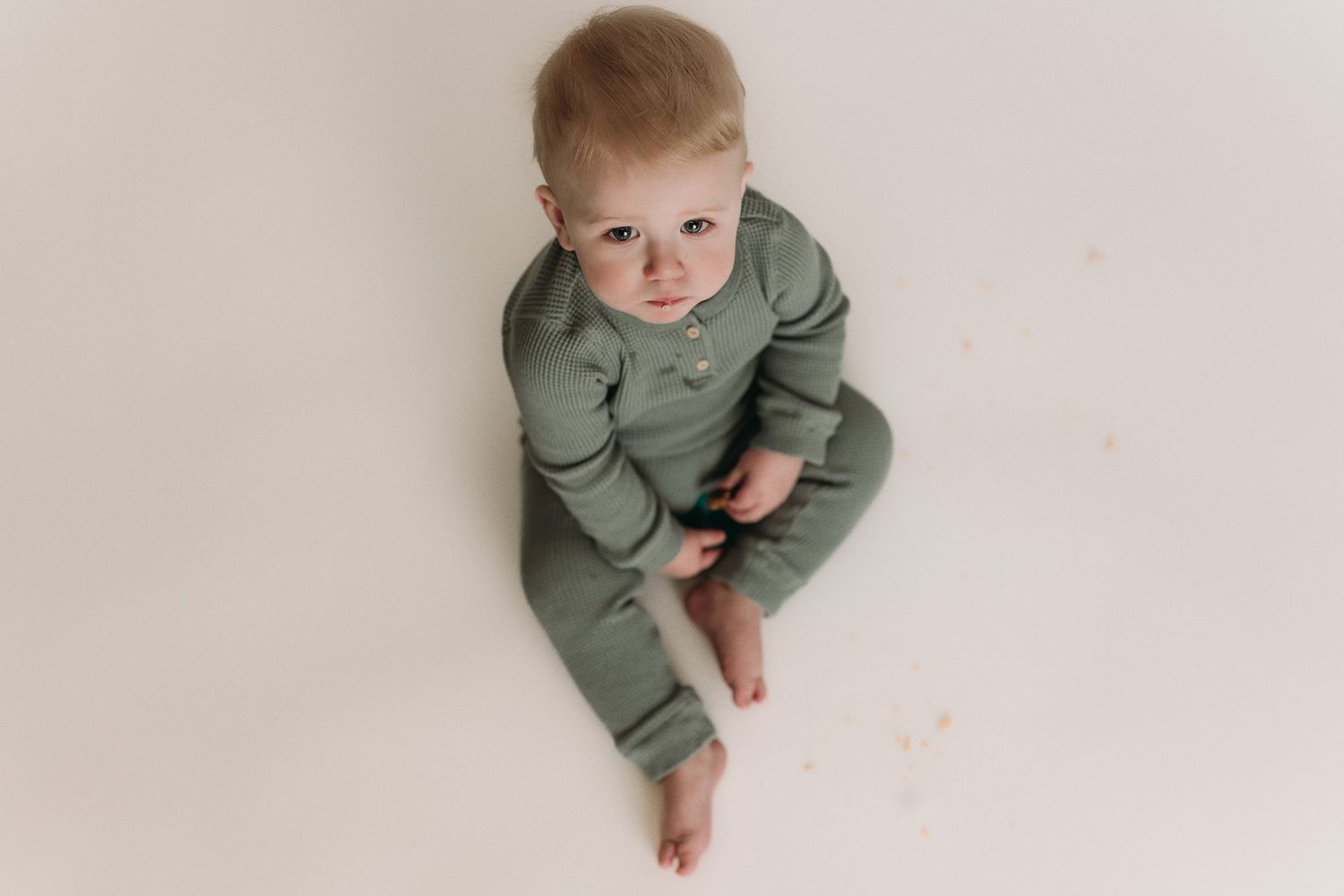 Baby in green knitwear poses for portrait against neutral backdrop.