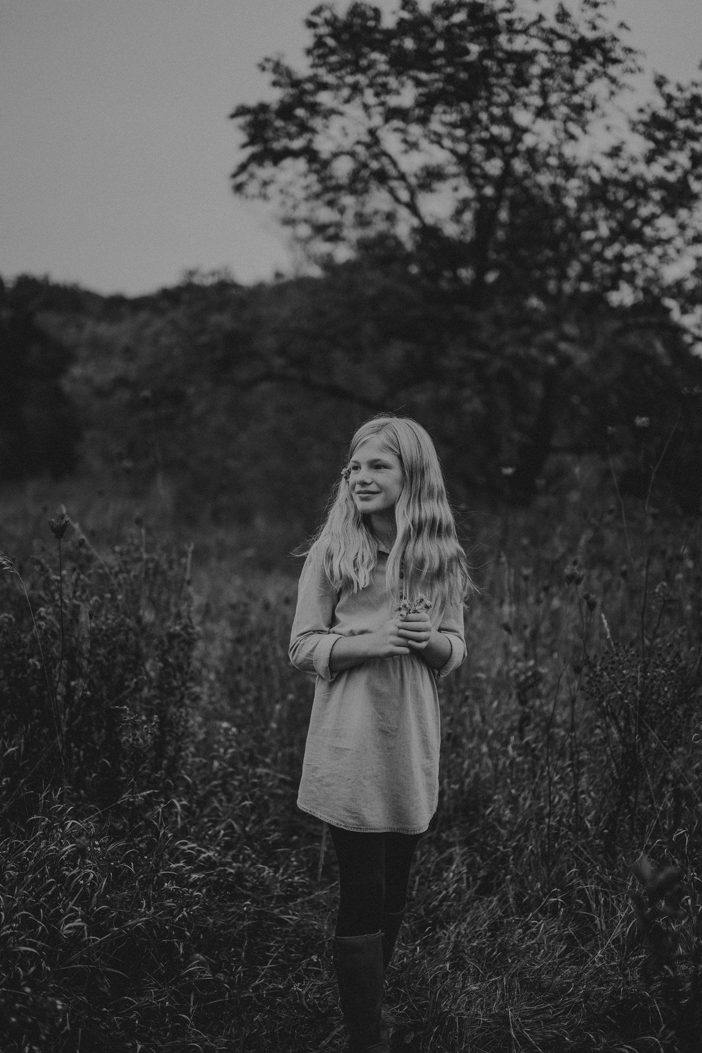 A figure stands in a meadow at dusk wearing a dress in this artistic black and white portrait.