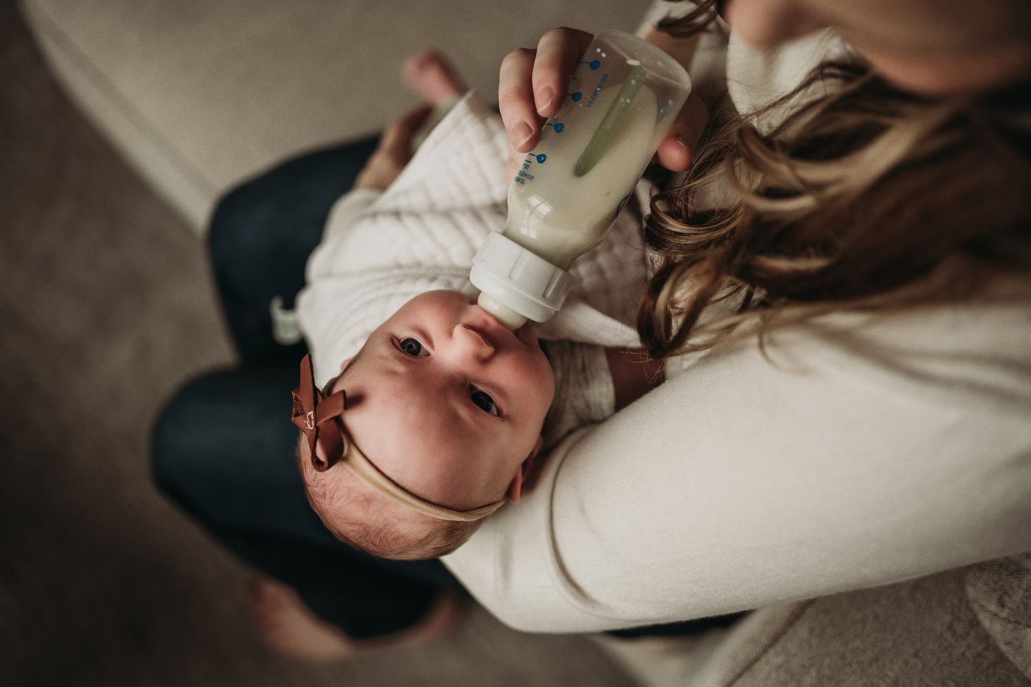 Overhead view of parent feeding newborn baby with bottle on couch.