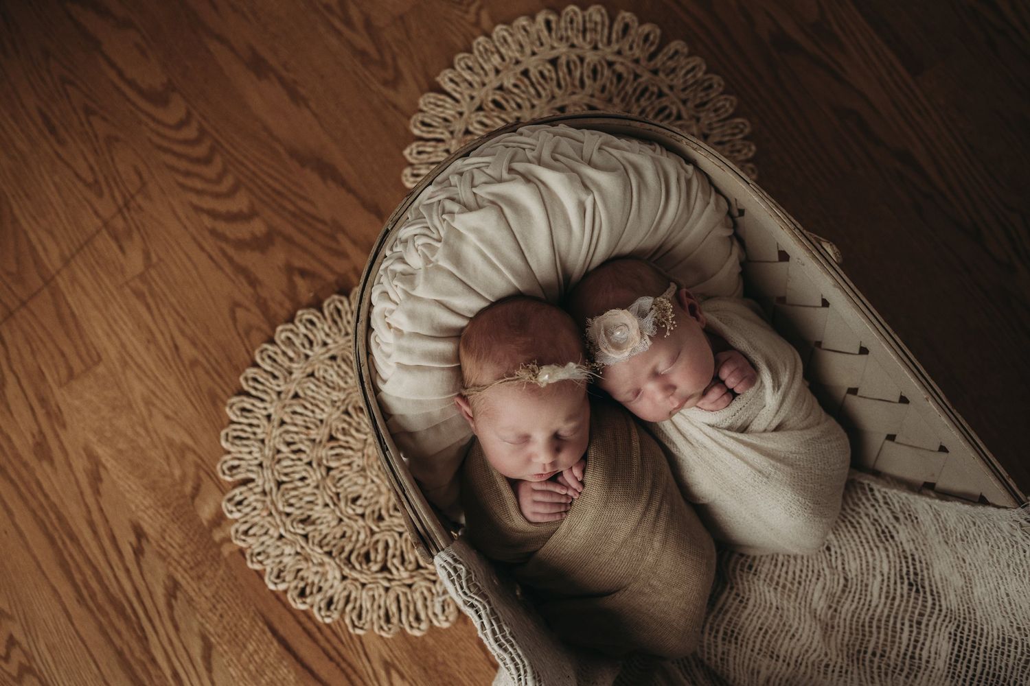 Overhead view of twin babies wrapped in neutral-colored swaddles lying in an ornate bassinet.