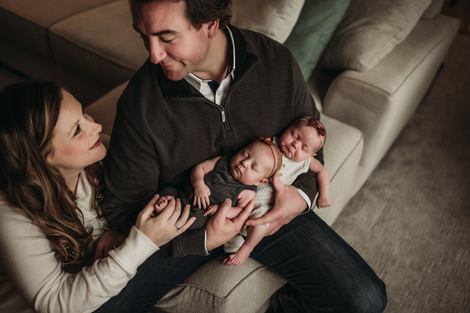 Couple sitting together on couch lovingly cradling their newborn baby.