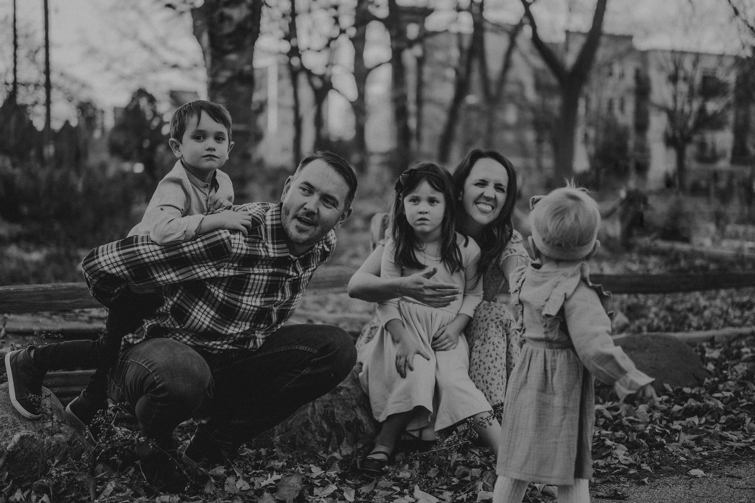 A candid black and white family photo taken outdoors on an autumn day.