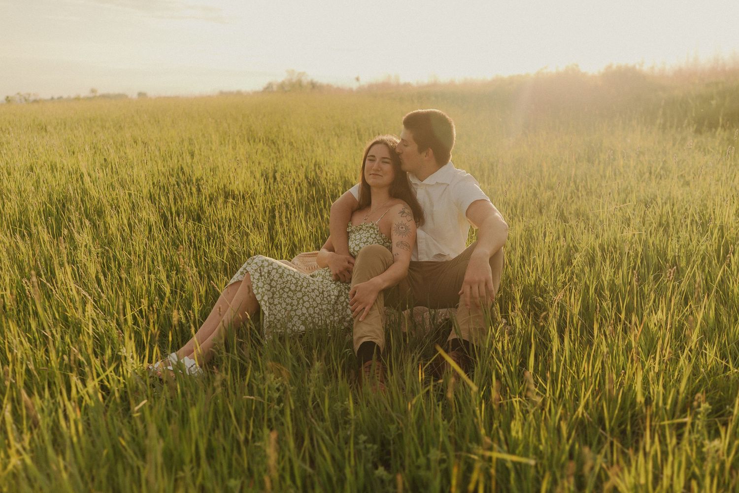 Couple sitting together in a sunlit wheat field during golden hour.