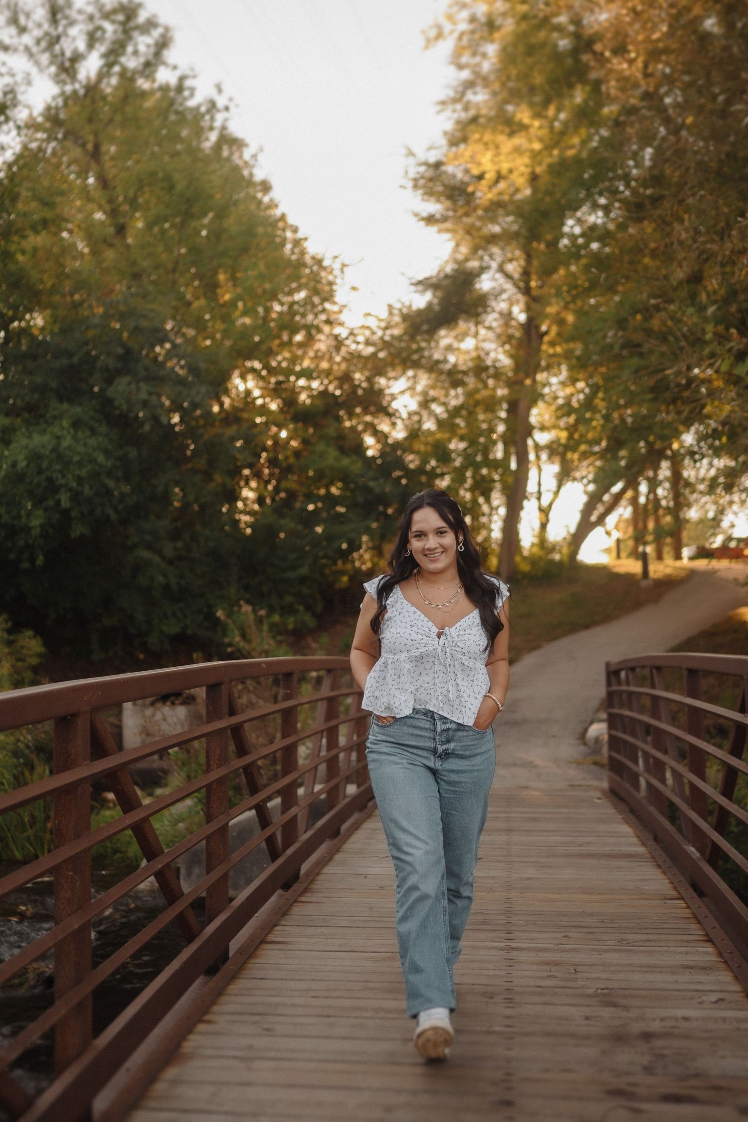 A person walks along a rustic wooden bridge surrounded by autumn trees during golden hour.