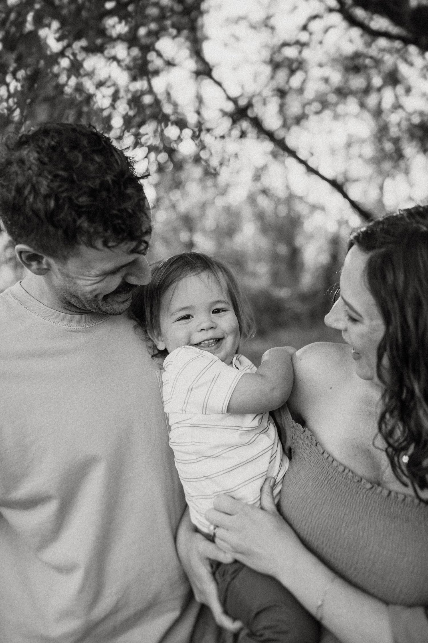 Black and white intimate family portrait capturing genuine laughter and joy outdoors.