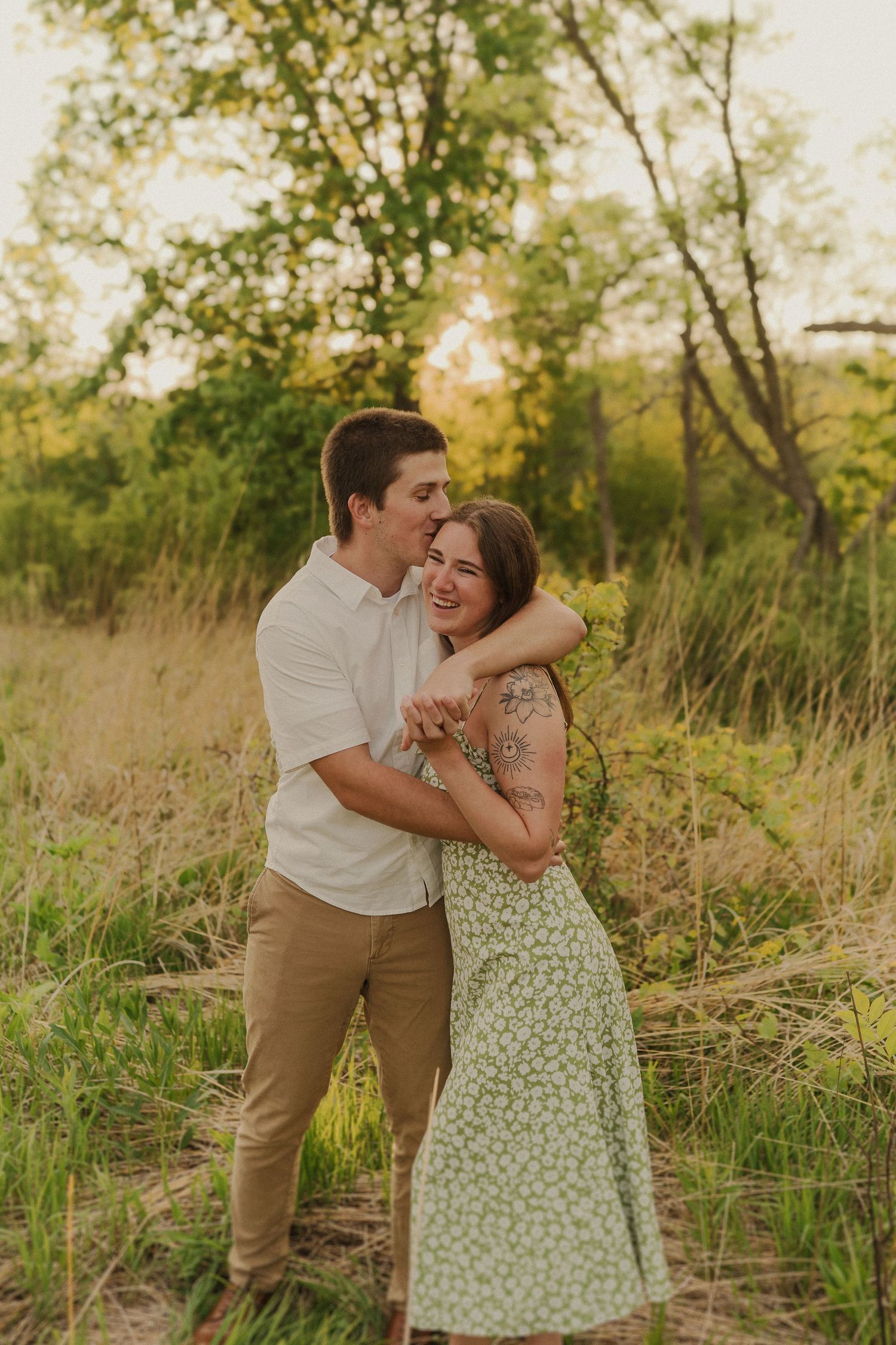 A couple shares a tender embrace while laughing together in a sun-dappled field.