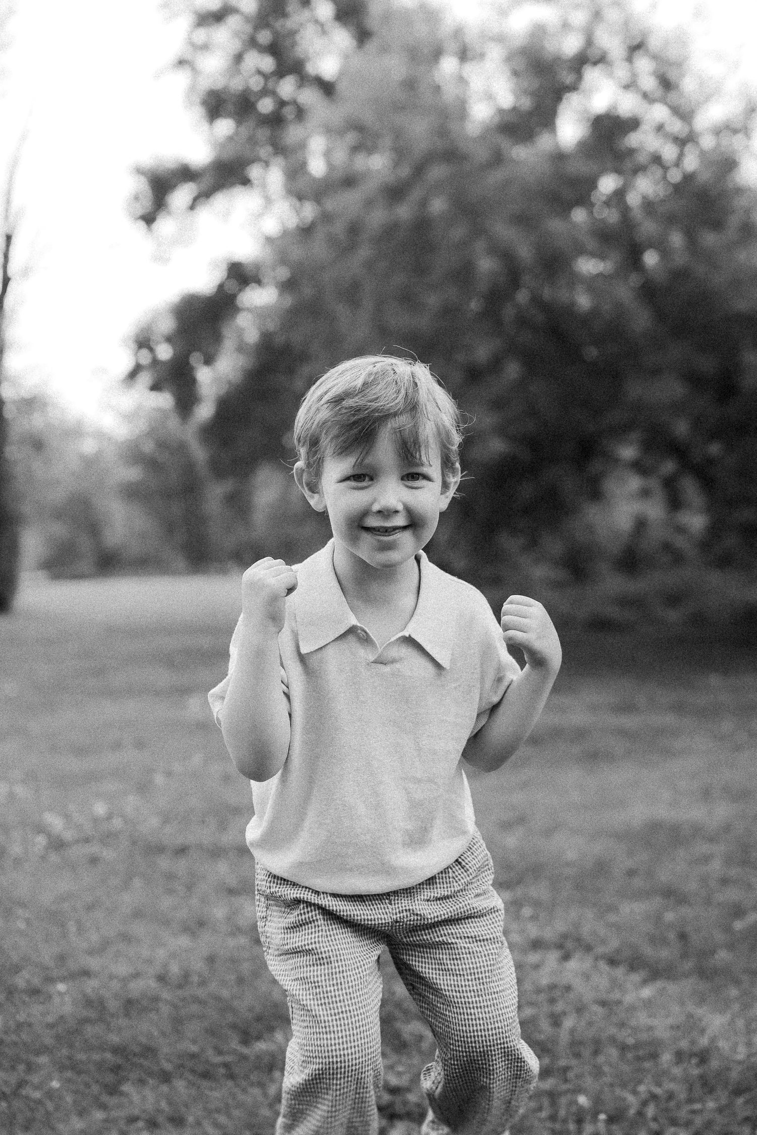 A black and white portrait of a young child running and smiling outdoors.