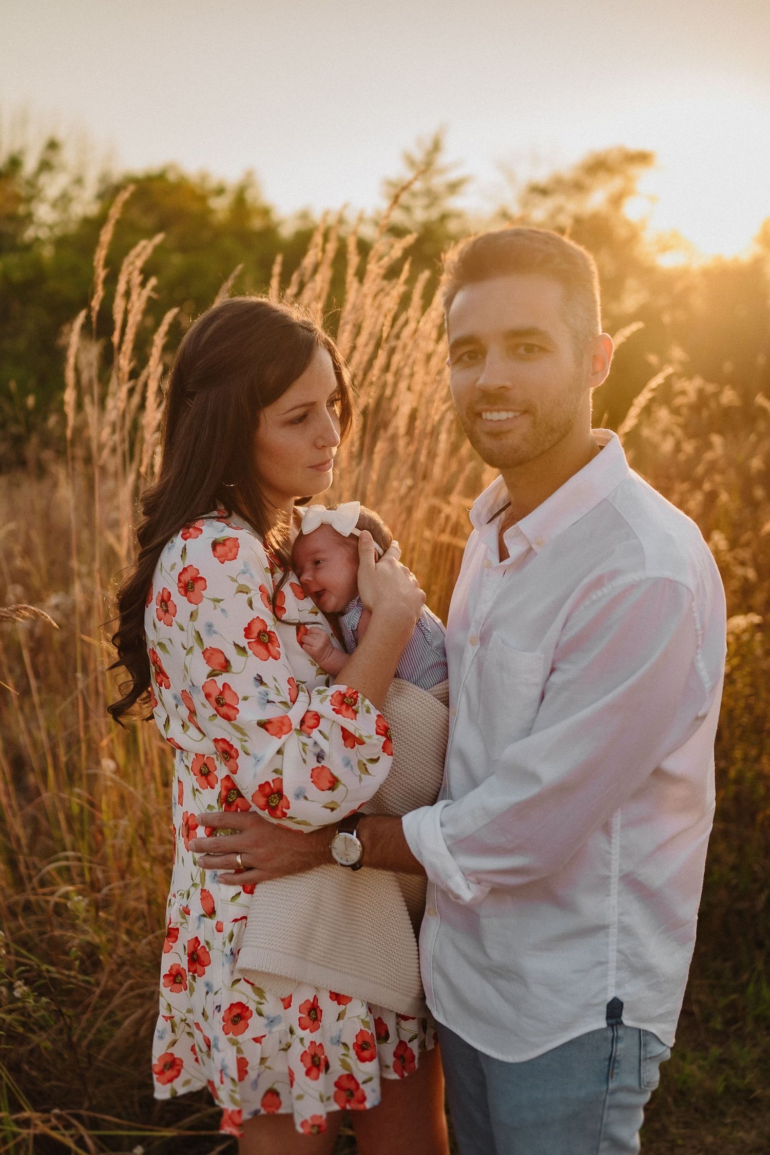 Family portrait at sunset with floral dress and white shirt among tall grasses.