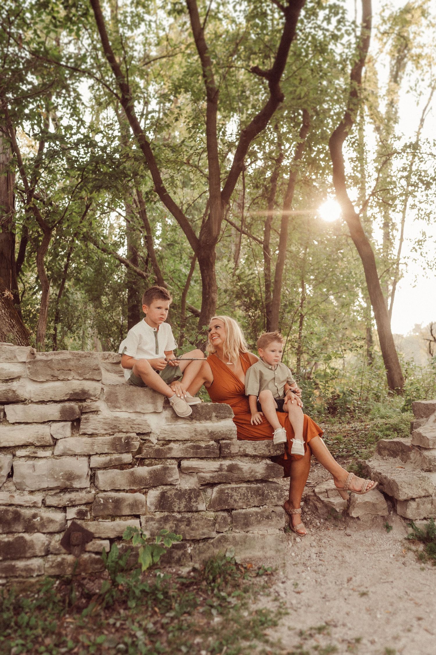Three people sitting on stone steps in a forest at sunset with golden light filtering through trees.