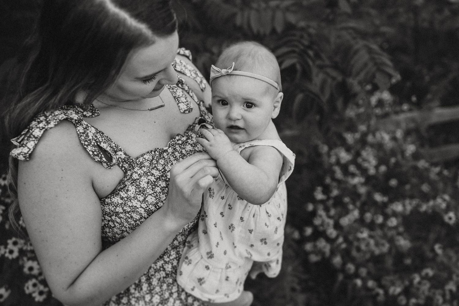 A gentle black and white portrait of a mother and baby outdoors among flowers.