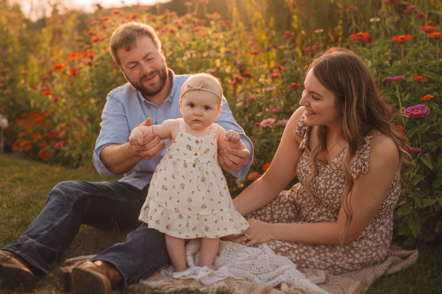 A family relaxes on a blanket in a garden with blooming red flowers during golden hour sunset.
