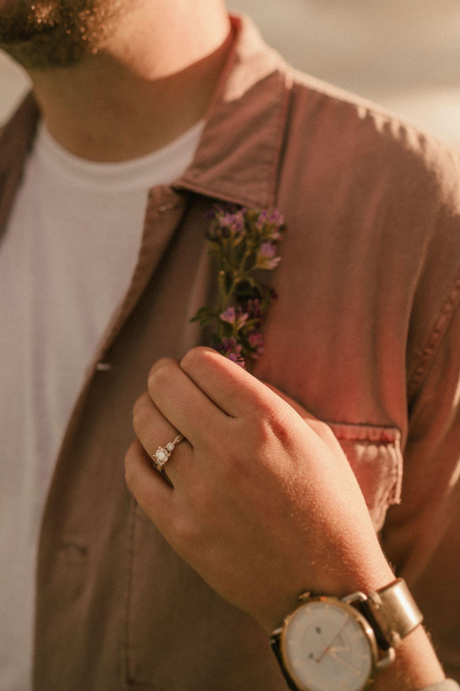 Detail shot of a pink jacket with boutonniere and engagement ring in warm sunlight.