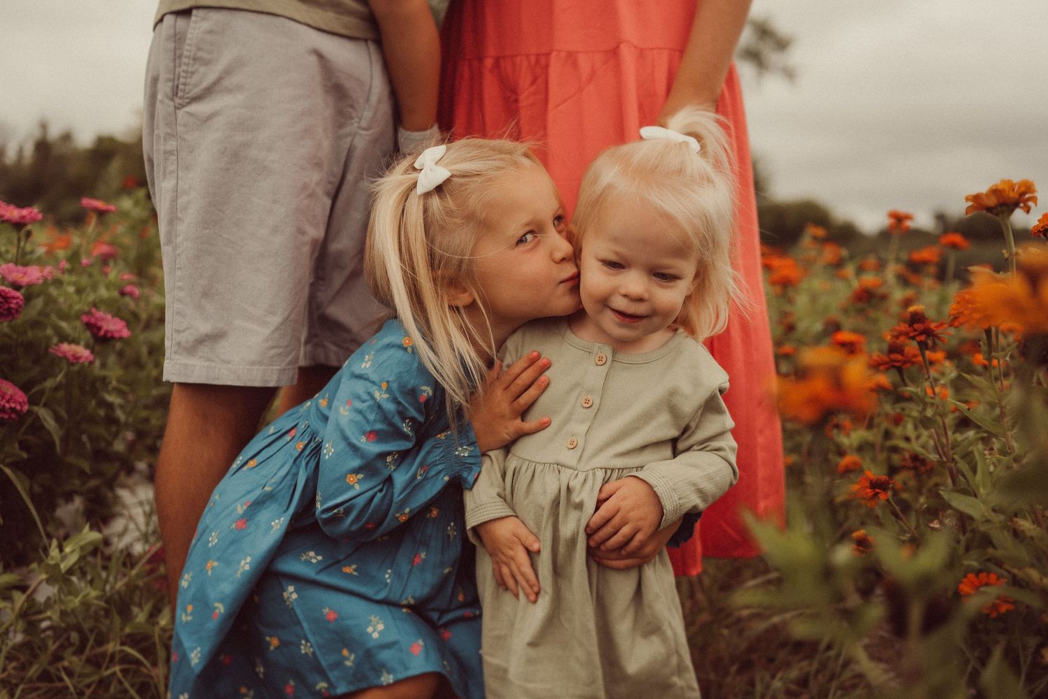 Two figures share a sweet moment while standing together in a garden filled with orange and pink flowers.