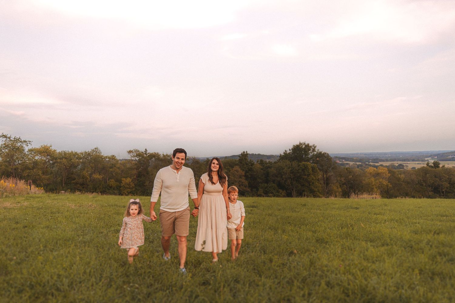 Family walking hand in hand through a countryside meadow at dusk.