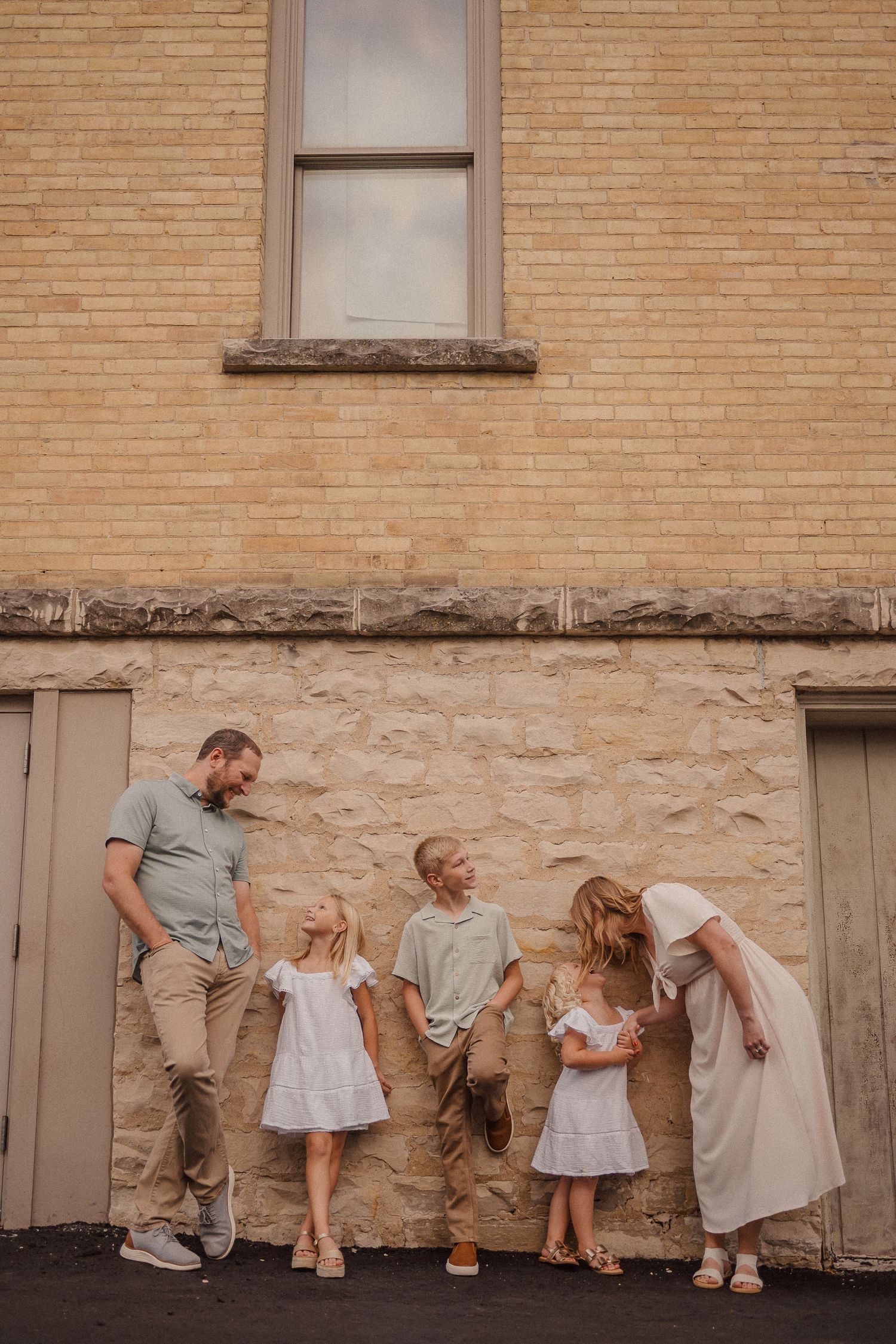 A playful sequence of poses against a brick wall shows coordinated casual outfits in neutral tones.