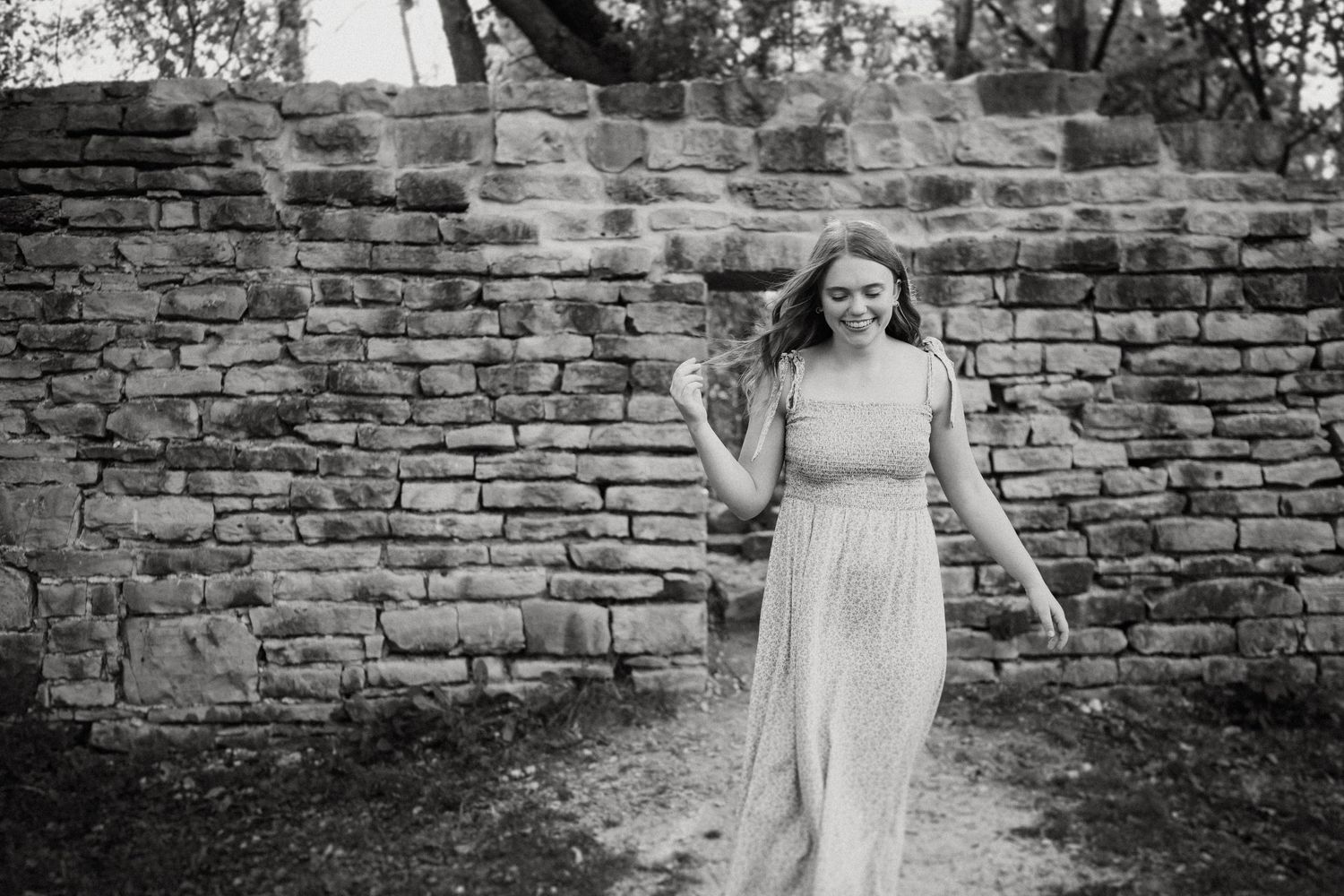 A carefree woman in a flowing dress walks in front of a rustic brick wall outdoors.