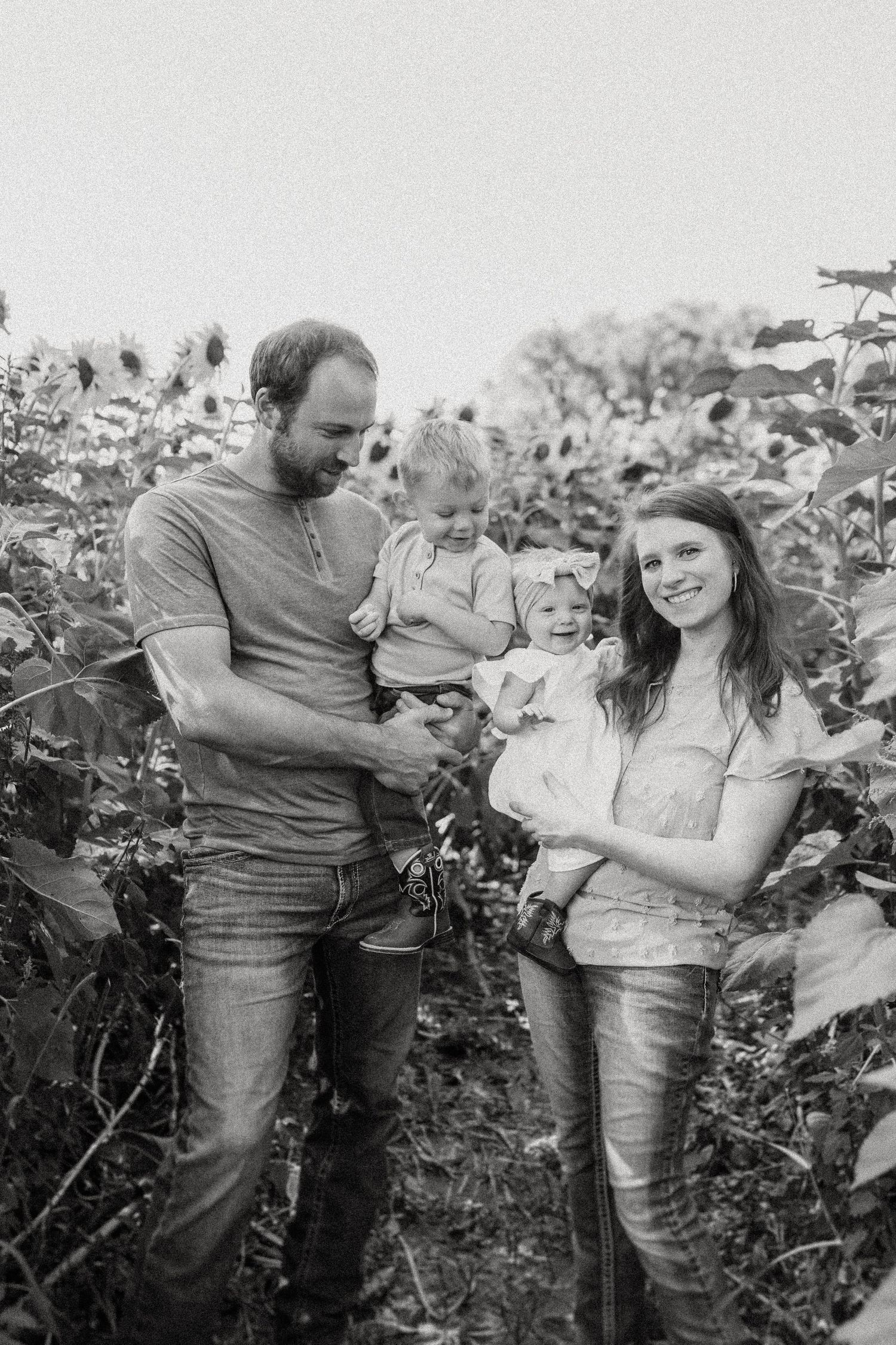 Black and white portrait of a family standing together in a sunflower field.