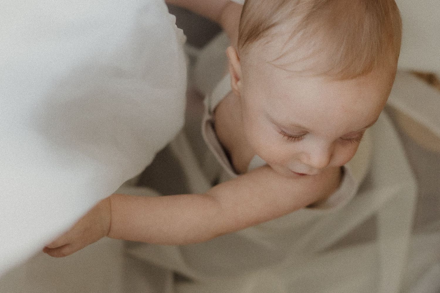 An adorable baby plays with flowing white curtains in natural lighting.