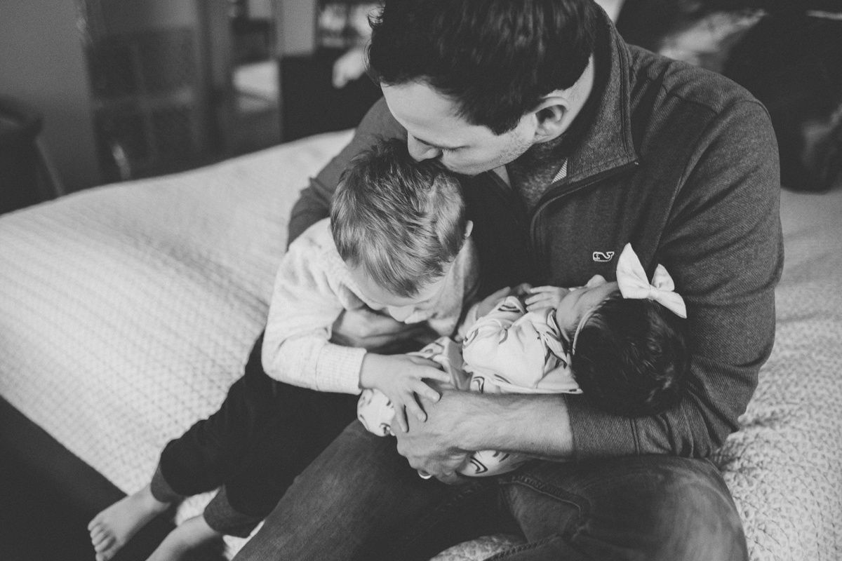 A tender black and white family moment showing affection with a baby and toddler on a bed.
