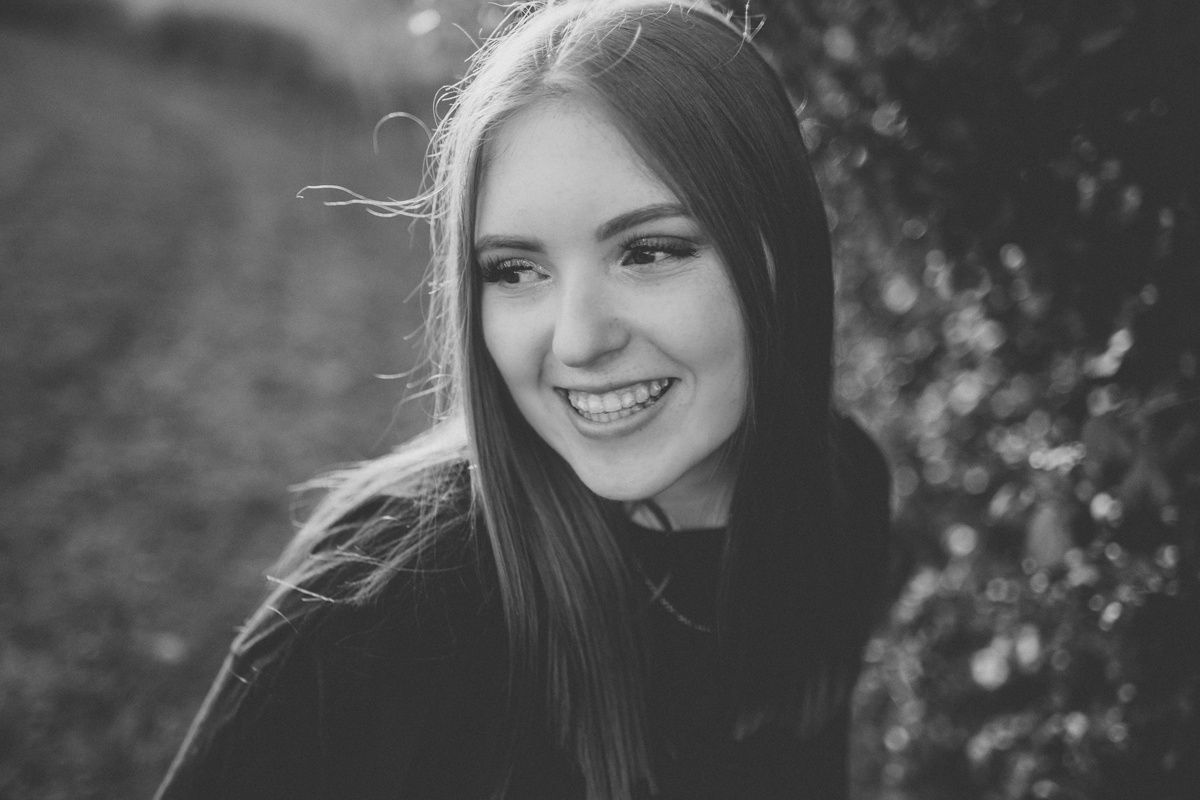 Black and white portrait with a gentle smile against natural foliage.