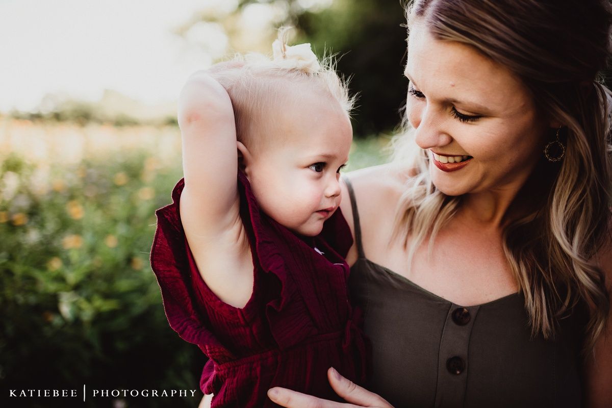 Sweet moment between parent and baby in burgundy dress during outdoor photoshoot.