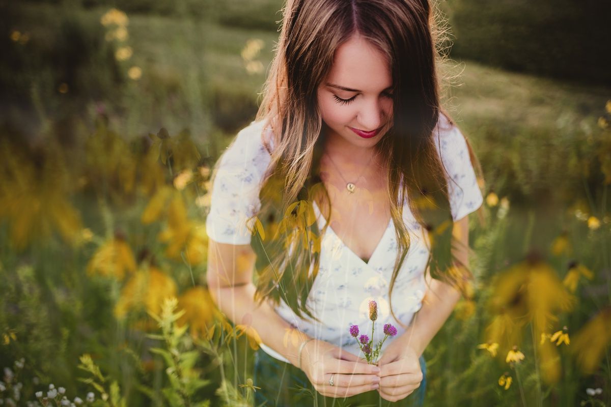 A gentle scene of a woman in a white top admiring wildflowers in a sunlit meadow.