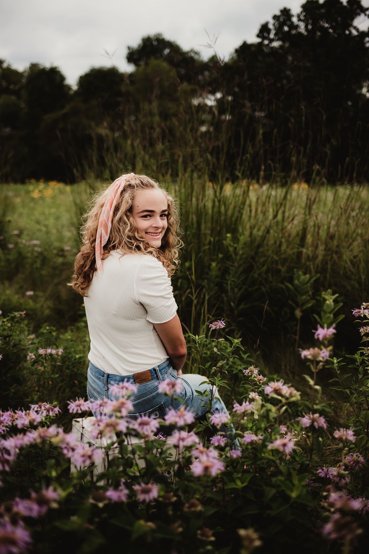 Portrait in a wildflower meadow with pink blooms and tall grasses at sunset.
