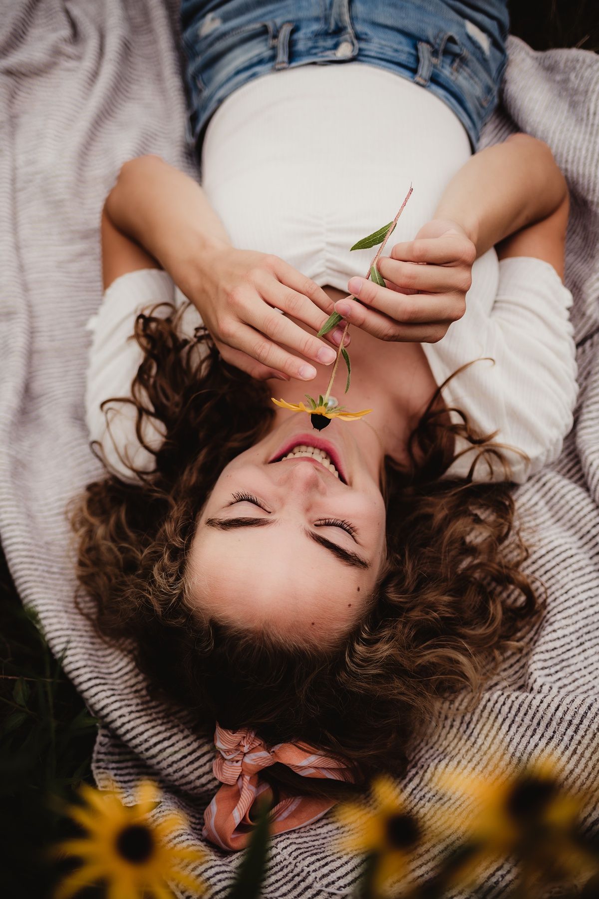 Artistic portrait of someone lying on blanket holding flower petals beside sunflowers.