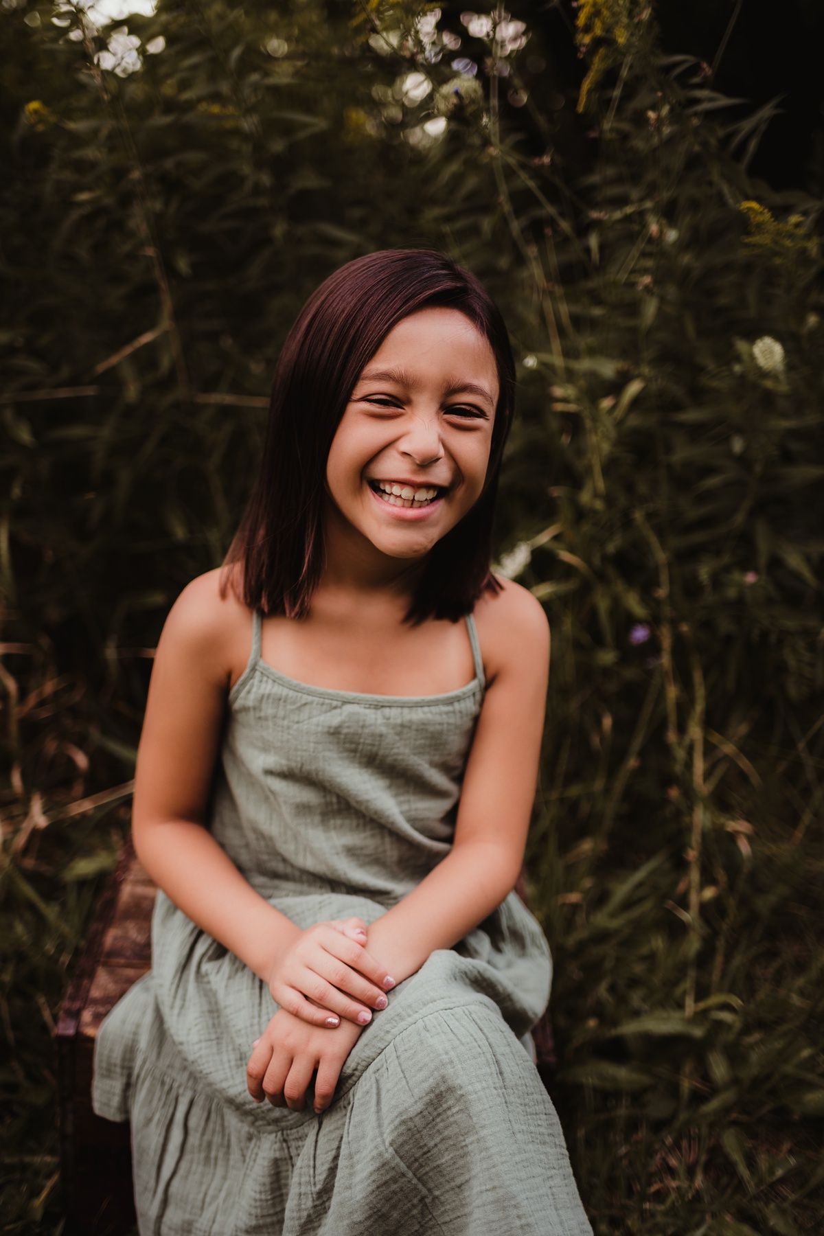 Portrait of a young girl wearing gray dress sitting outdoors with natural foliage background.