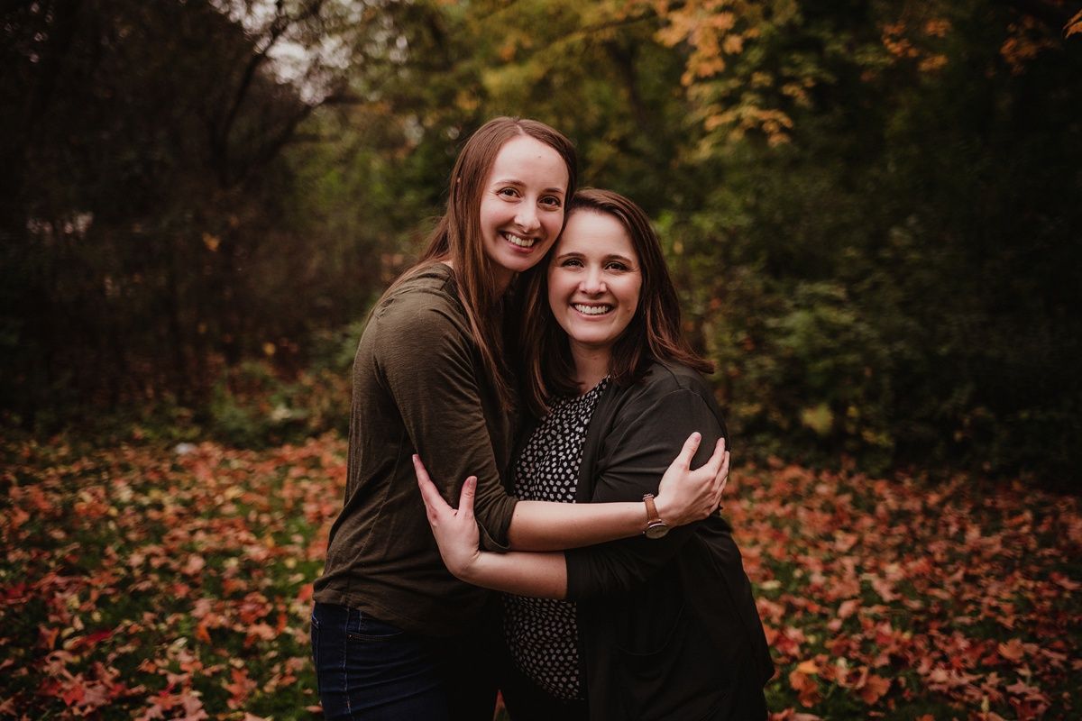 Two people sharing a joyful embrace outdoors with autumn leaves on ground.