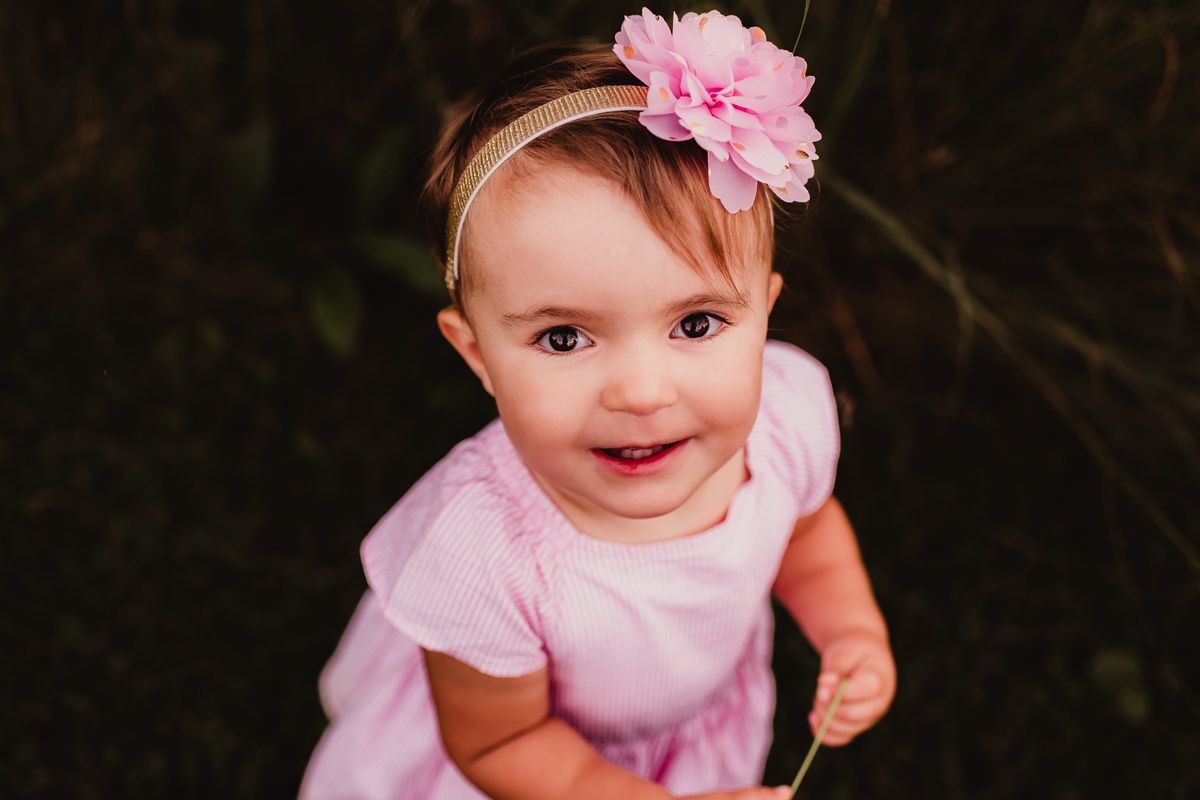 Sweet baby in pink outfit with flower headband smiling at camera.