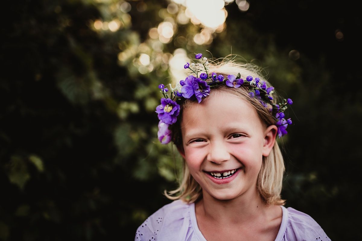 A joyful portrait of someone wearing a purple flower crown against a blurred natural background.