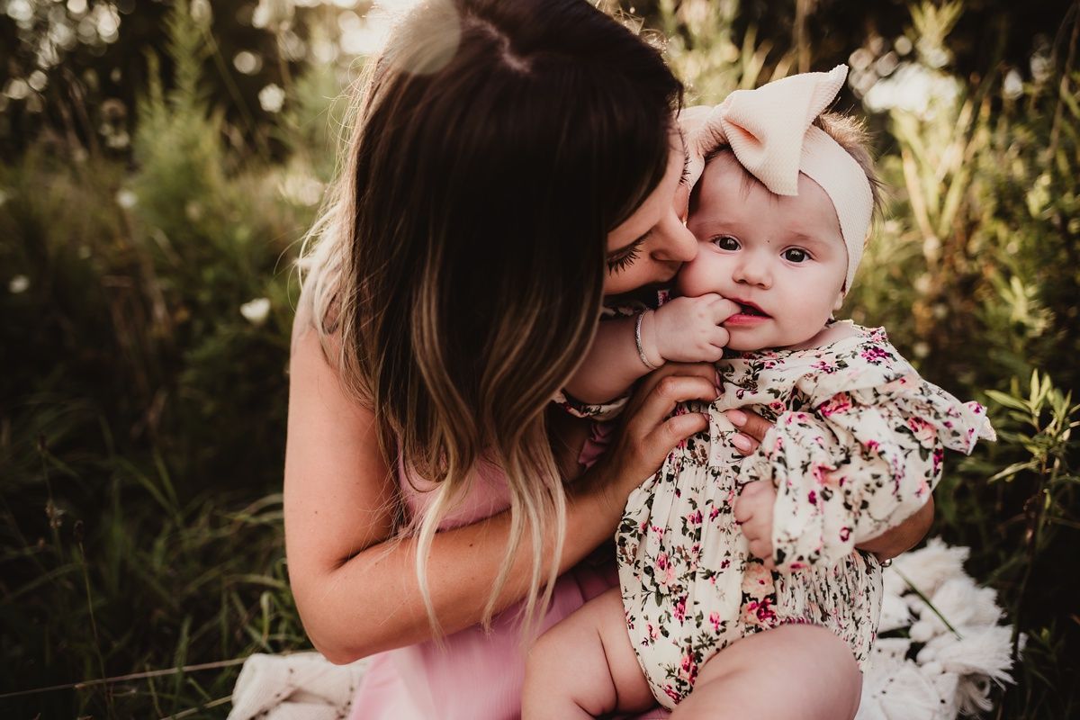 A tender moment between parent and baby outdoors with golden sunlight filtering through trees.
