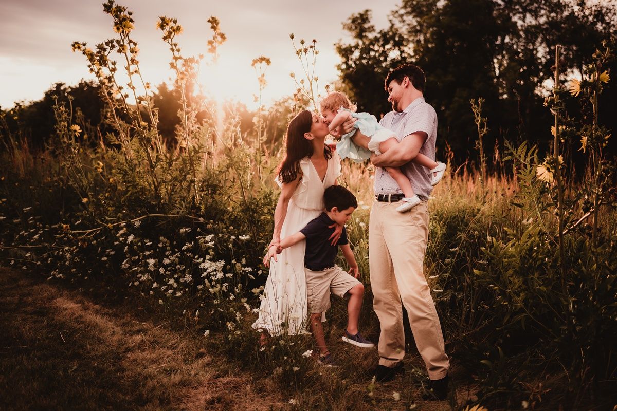Family enjoying playful moments in wildflower field at sunset.