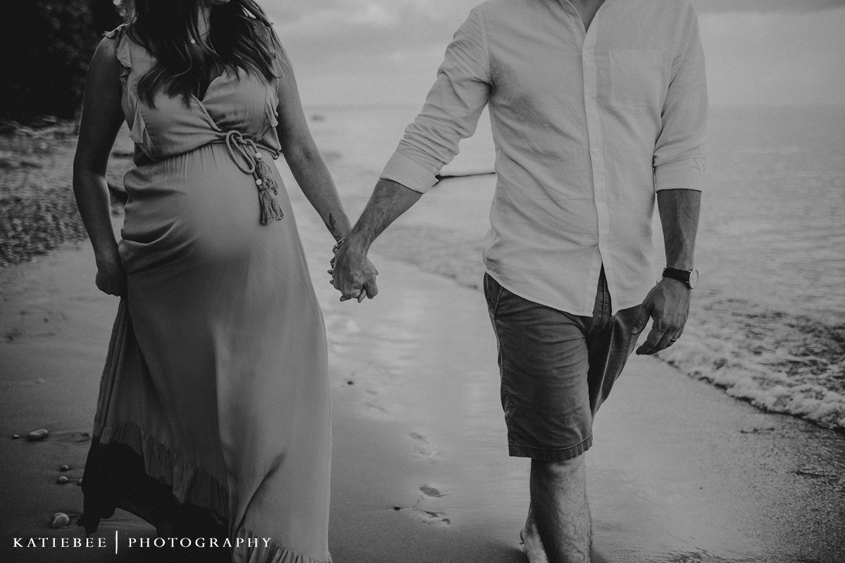 A couple holds hands while walking along a beach in black and white.