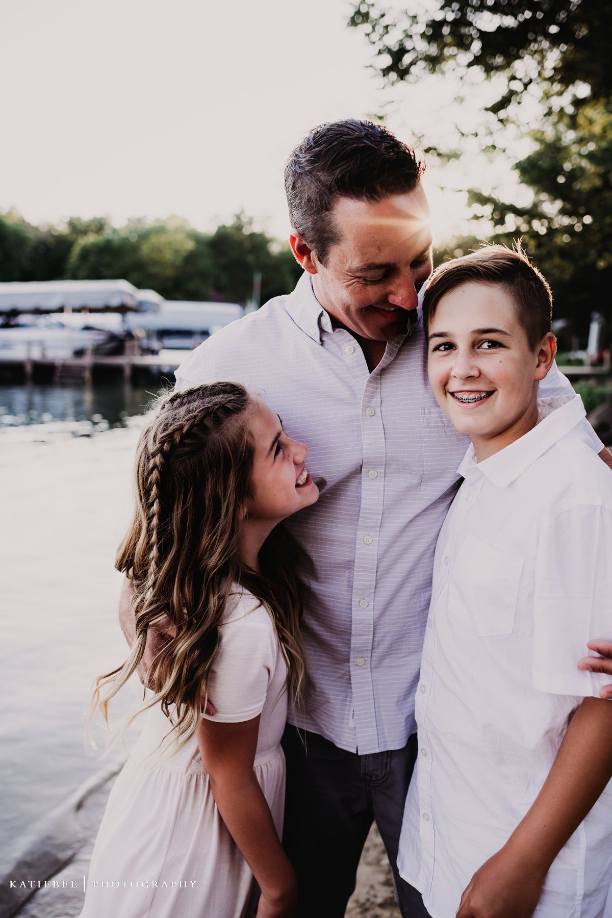Three people share a close moment together by a marina at sunset.