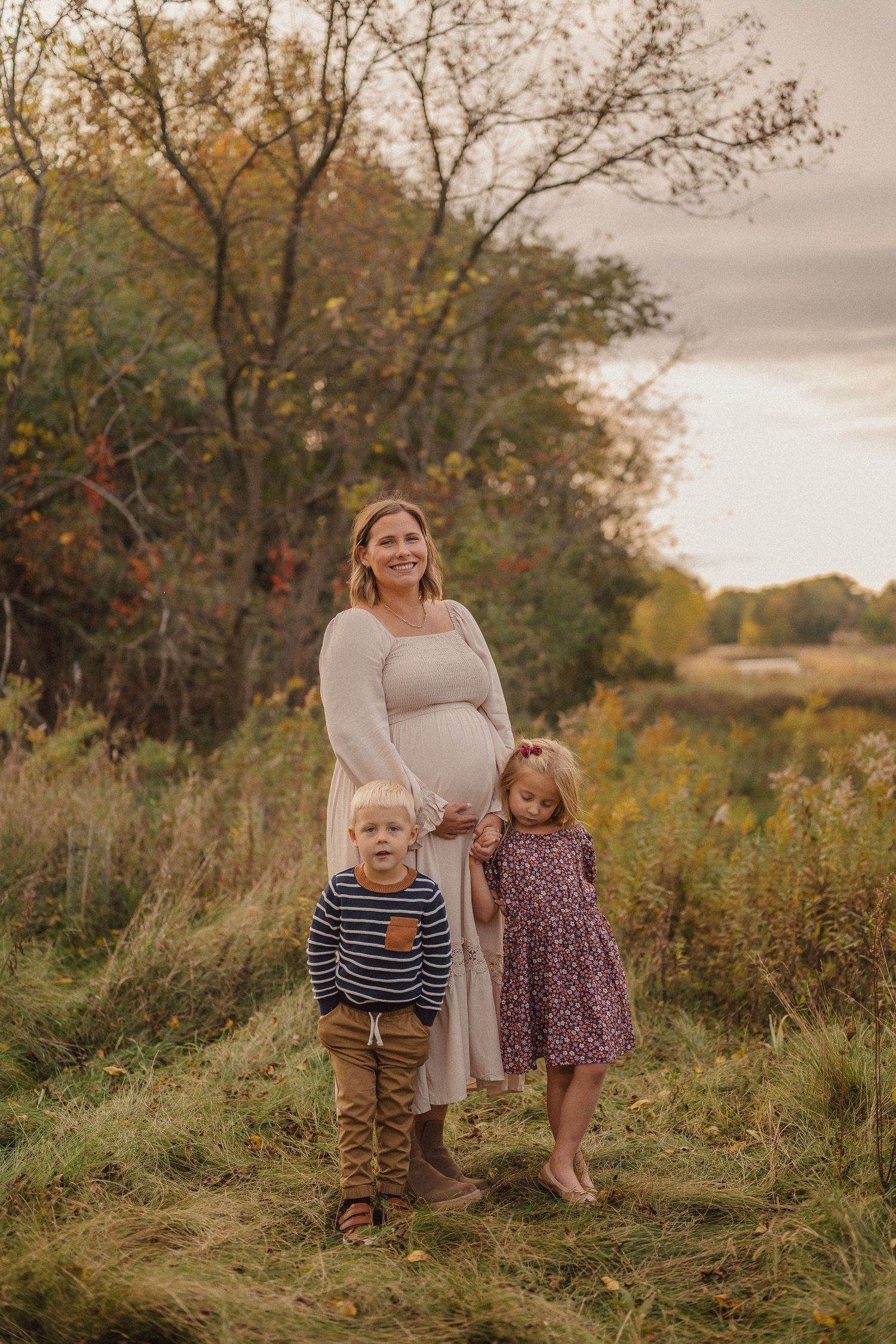 Family portrait in a rustic autumn field with tall grass and trees at sunset.