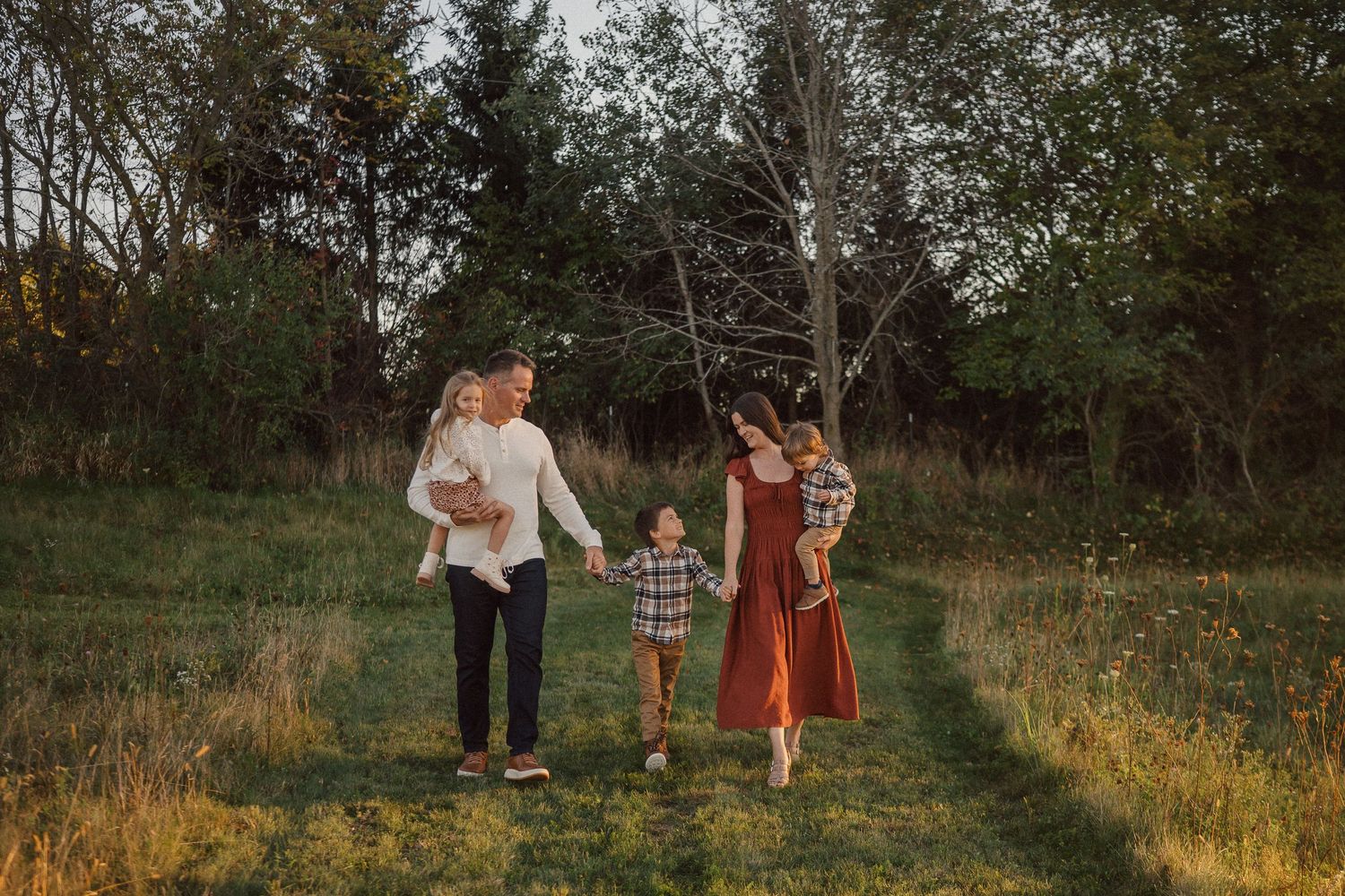 A family walks together through a golden autumn field during sunset, holding hands and enjoying nature.