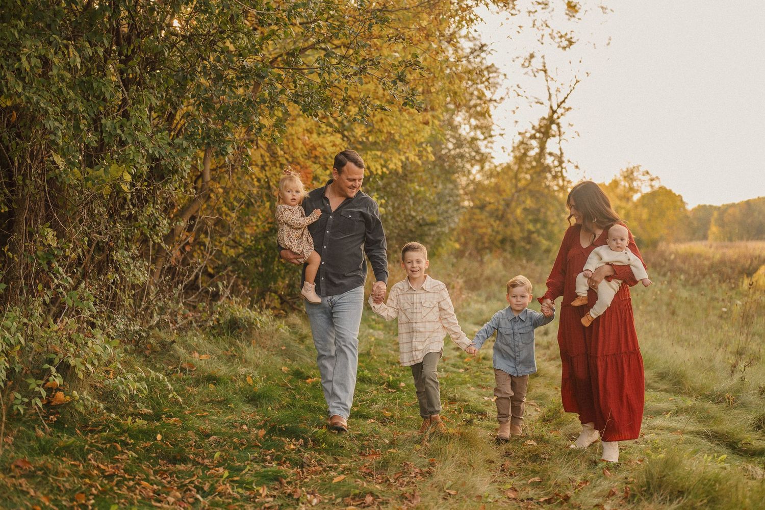 Family walking together through a golden autumn field at sunset with warm lighting and natural scenery.