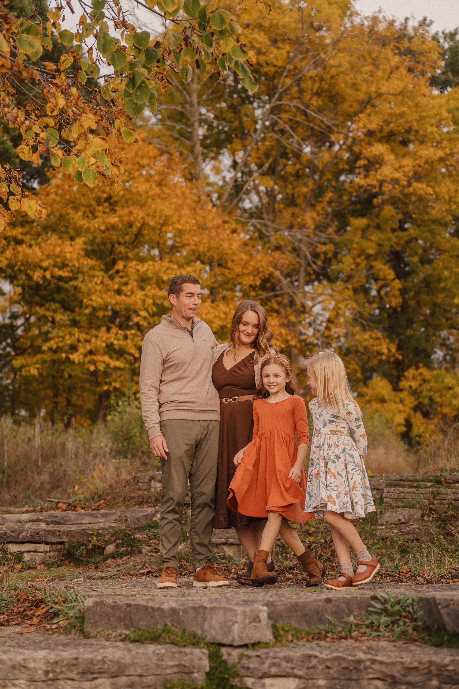 Family of four standing on stone steps surrounded by golden autumn trees.
