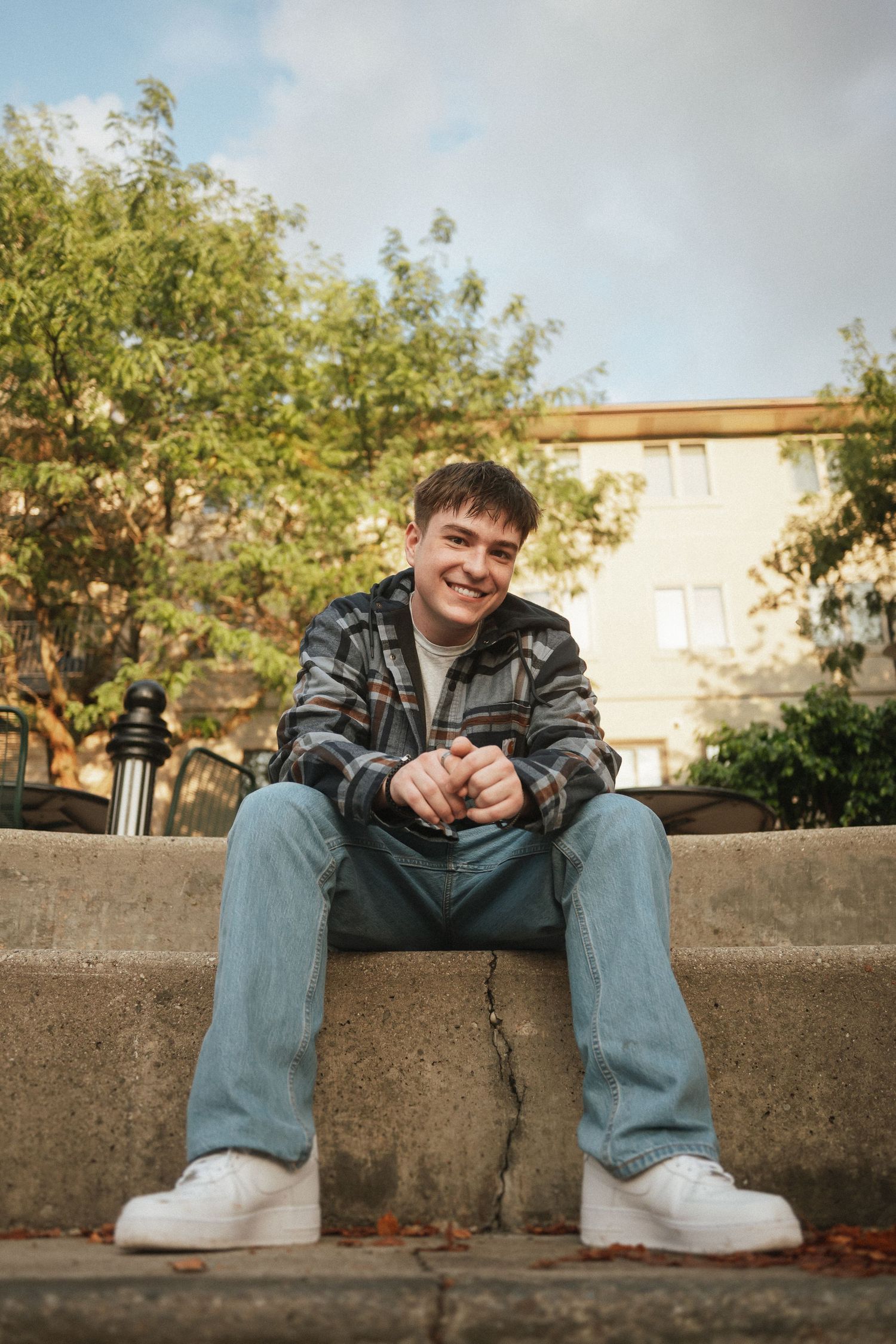 Person in denim and plaid jacket sitting casually on concrete wall during golden hour.