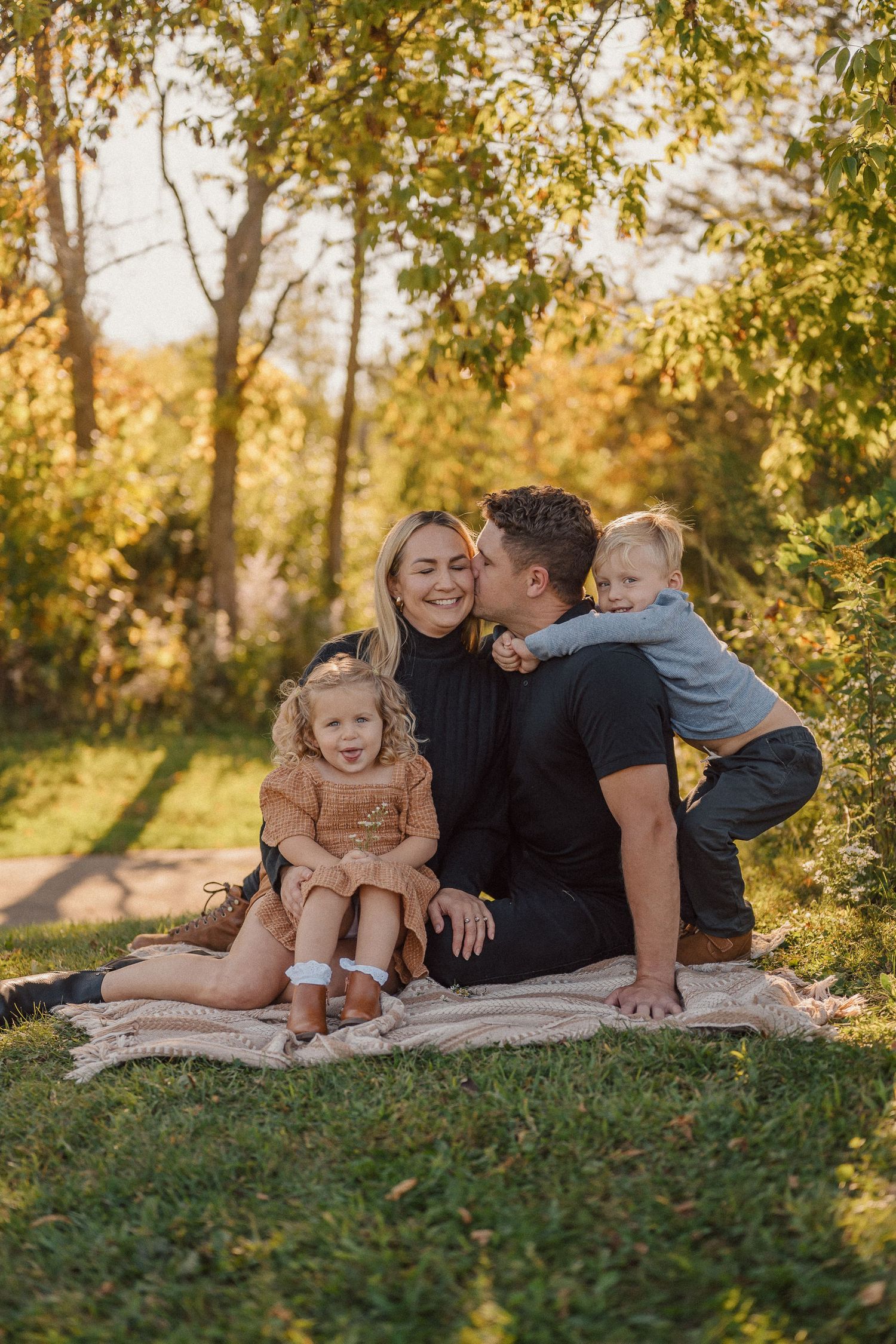 Family shares intimate moments while lounging on a blanket in a sunlit park setting.