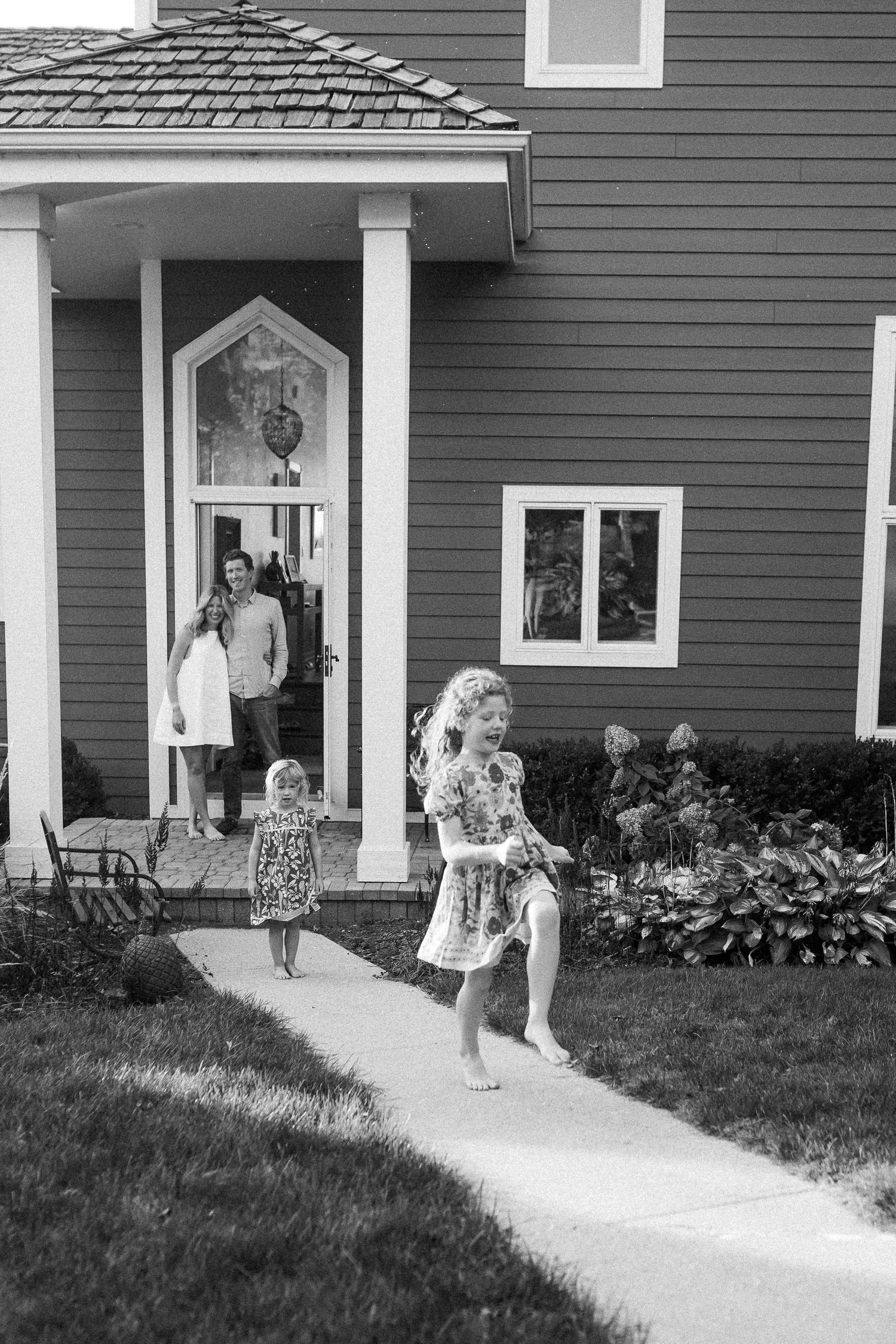 A series of black and white photos showing playful moments on a front porch with hydrangea bushes.
