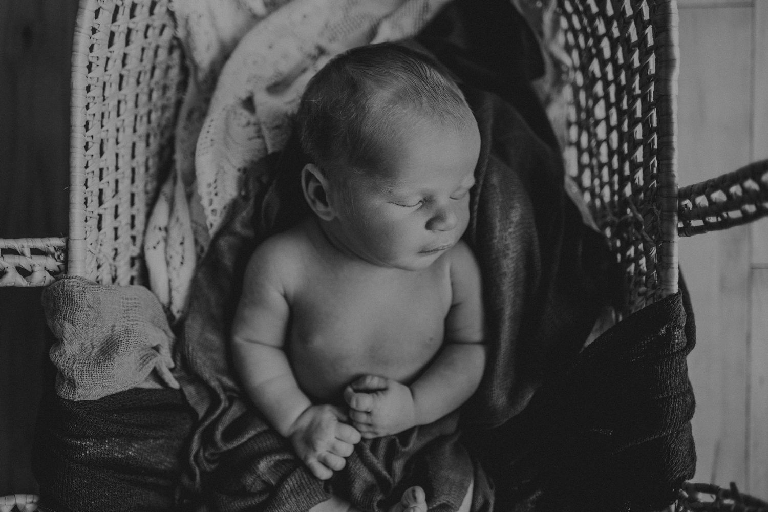 Black and white portrait of a newborn baby sleeping in a wicker basket.
